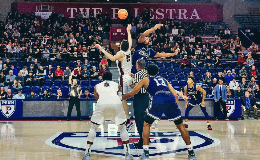 two players jumping for a ball with fans in stands behind