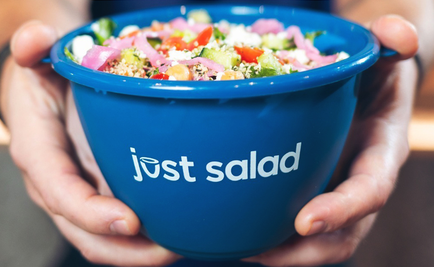 hands holding blue bowl filled with salad