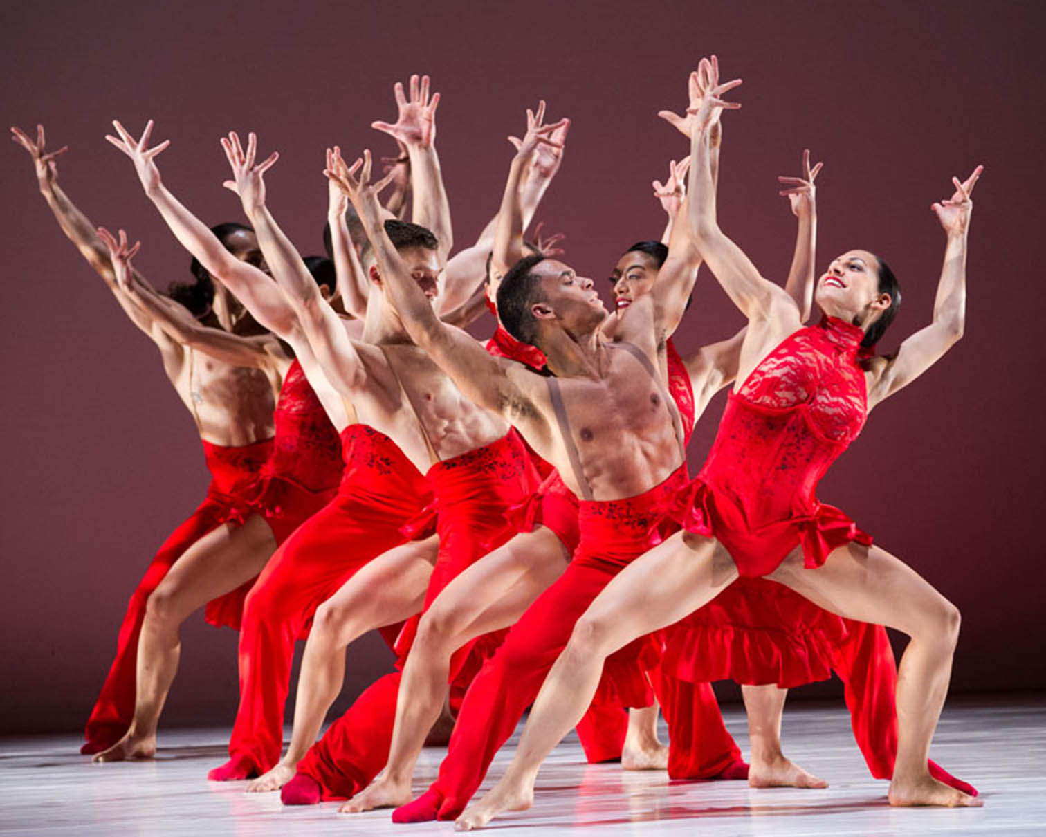 ballet dancers on stage in red costumes with arms raised