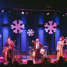 December Playlist singers on stage with snowflakes hanging above