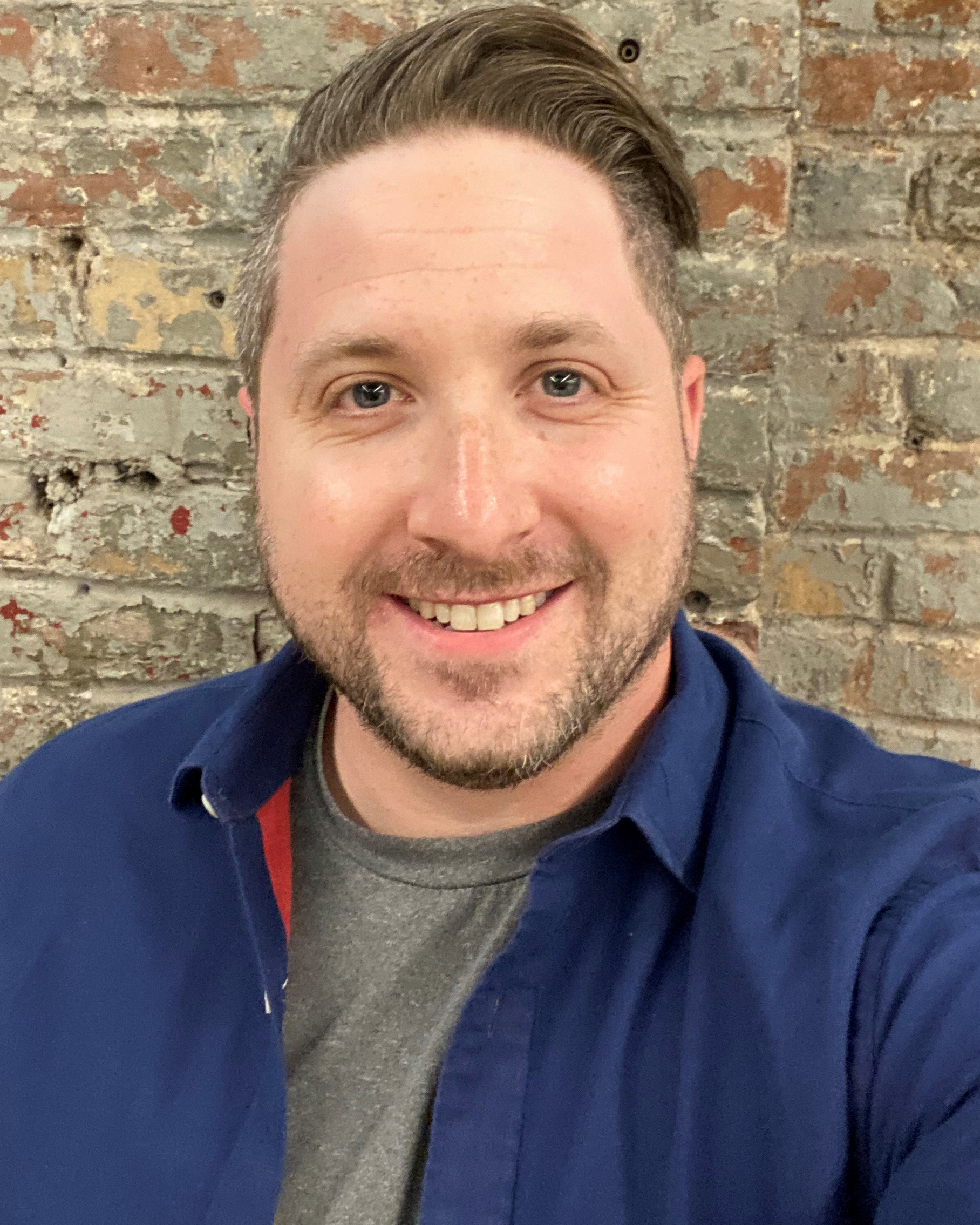 smiling man in front of brick wall