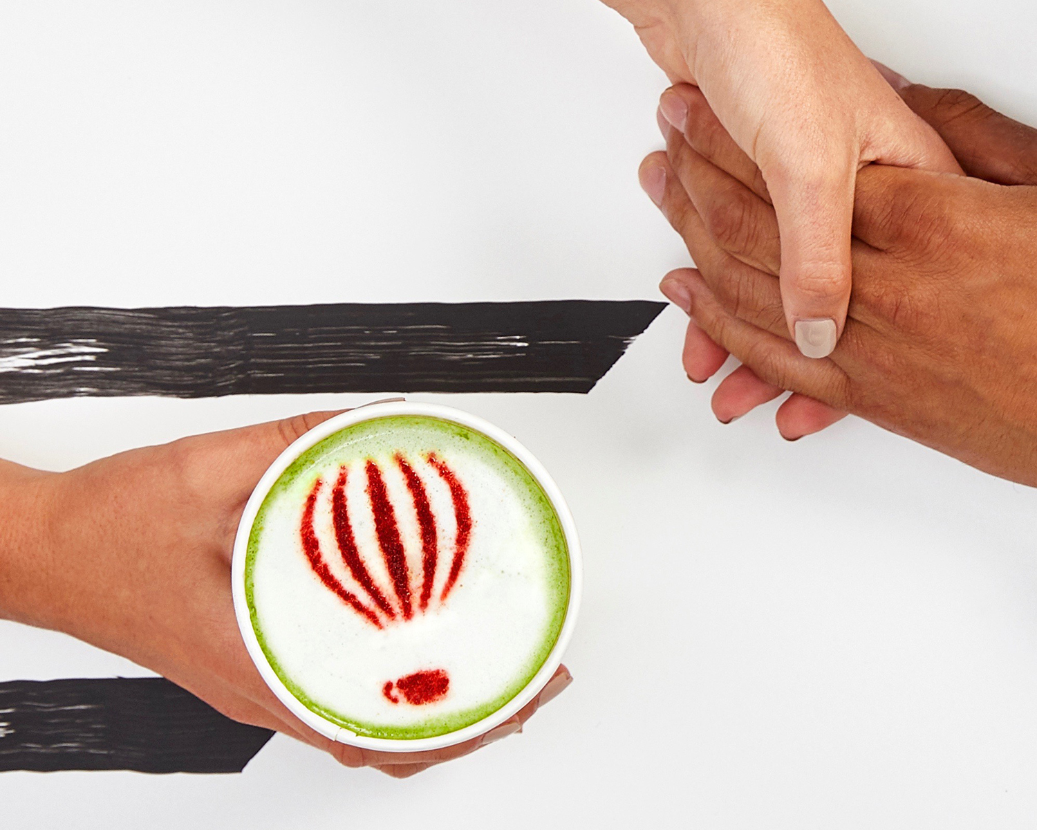 two hands holding and cup of matcha coffee with red heart on top
