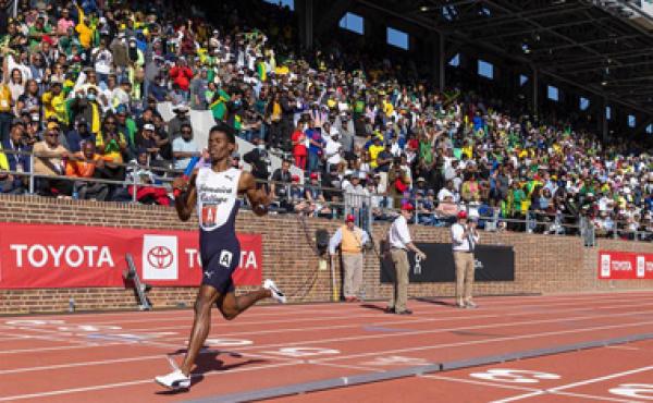 runner crossing the finish line in front of a stadium crowd