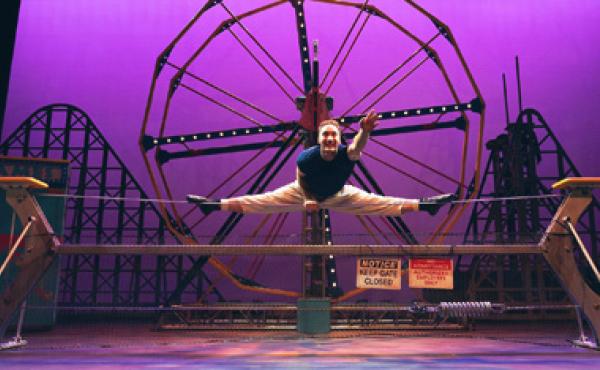 cirque performer on a tightrope in a split reaching out towards the audience