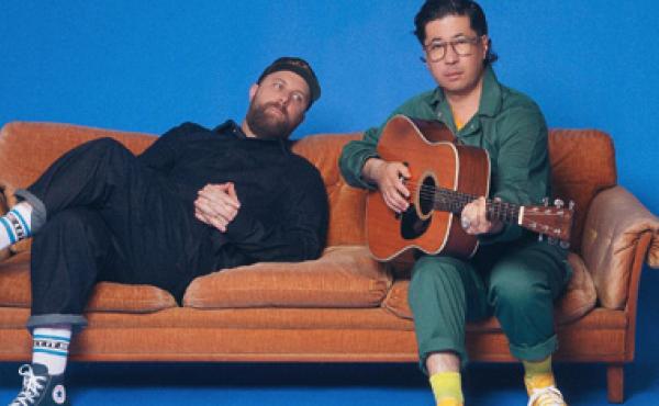 two men sitting on a couch and one holding a guitar