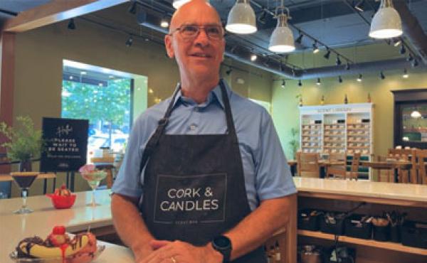 bald man in an apron that says Cork & Candles