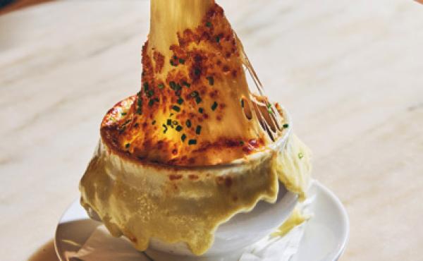 bowl of french onion soup with the cheese being pulled up