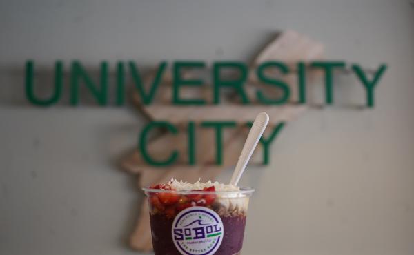 Image of an acai bowl in front of University City sign 