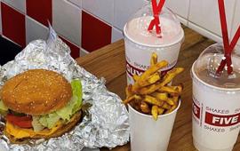 a cheeseburger, cup of fries and two milkshakes on a table